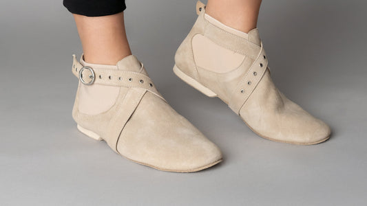 Beige suede ankle boots worn with black pants on a gray background